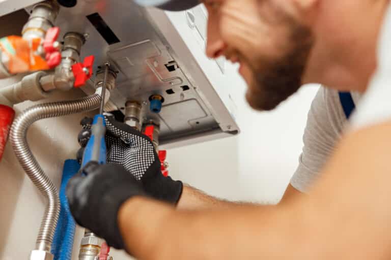 Closeup of plumber using screwdriver while installing new steel hot water central heating system in